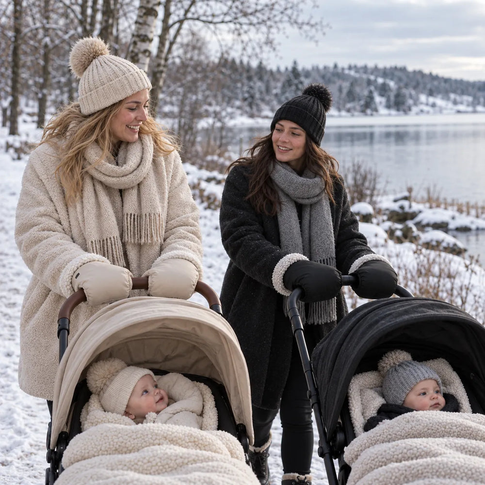Två mammor promenerar med barnvagnar vid en snöig sjö – den ena med beige och den andra med svarta Lovelle Cosy barnvagnshandskar